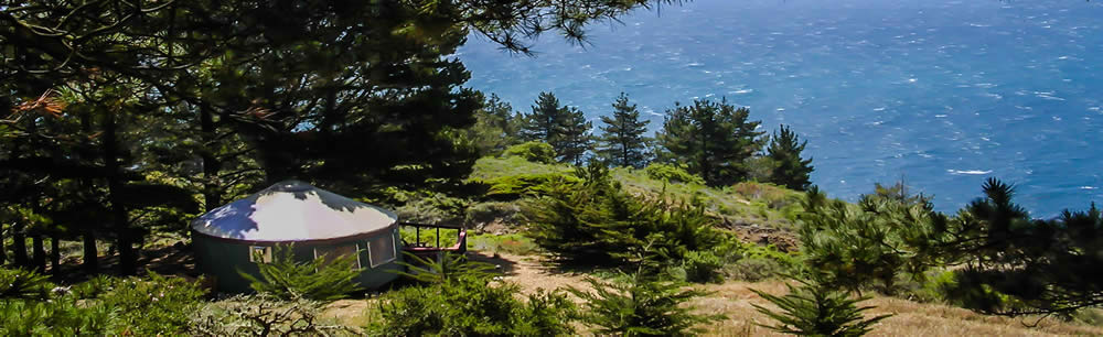 A grassy hill with a yurt overlooking the ocean.