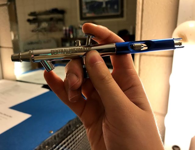 A blue airbrush held in a hand.